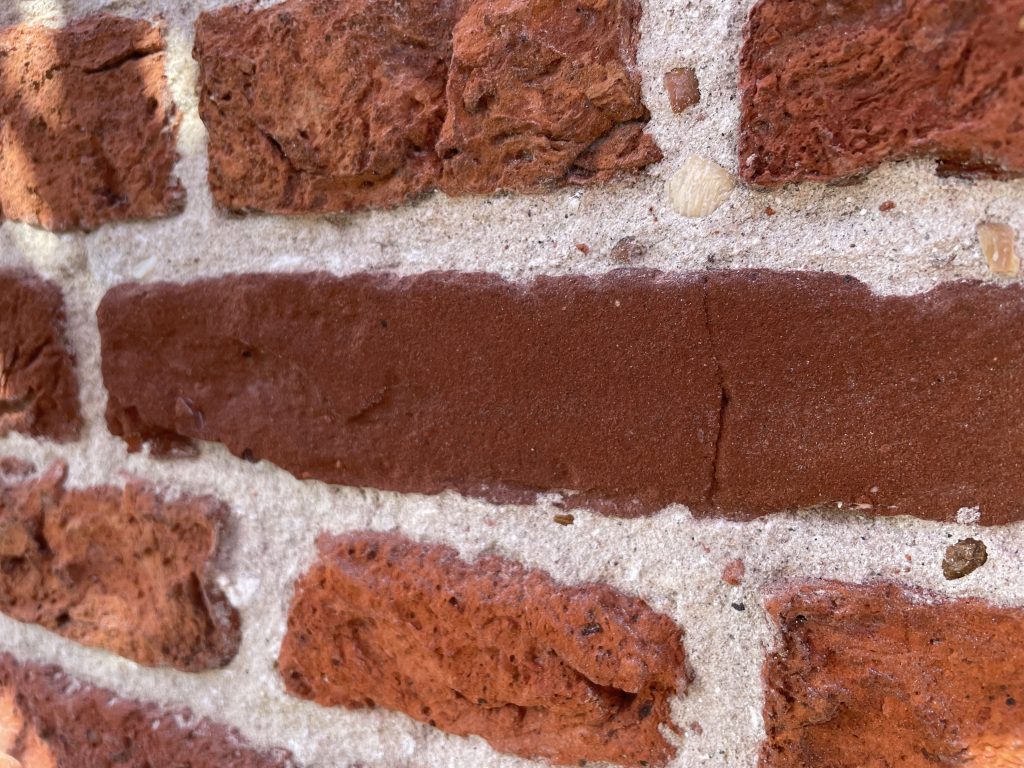Getamponneerde kalkvoeg met zichtbaar zand en grovere aggregaten tussen rood metselwerk.